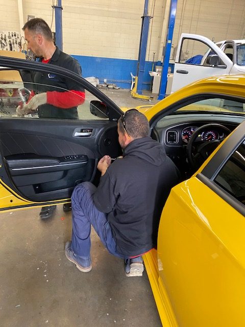 Auto Glass Force technicians working on a yellow car door